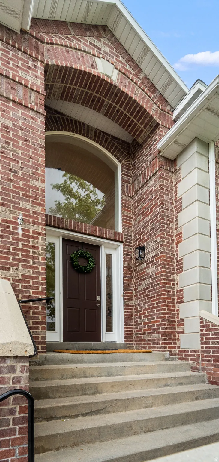 Brick exterior with an arched window, a paneled entry door, and concrete steps with a black metal railing