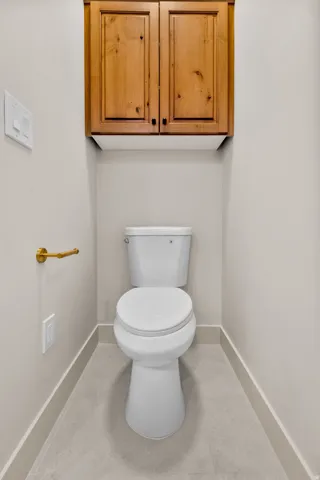 Recessed toilet with overhead wood cabinetry, gold-finish hardware, and tiled flooring