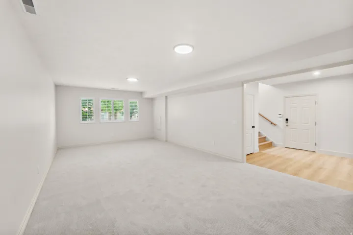 Spacious room with light-colored carpeting, multiple windows featuring plantation shutters, and recessed lighting