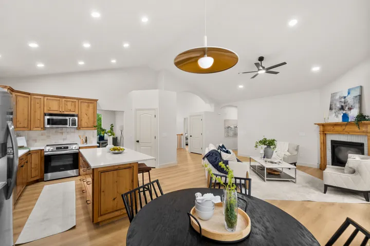 Vaulted ceilings, recessed lighting, wood-finish flooring, a kitchen island with stone countertops, and a fireplace with a wood mantle