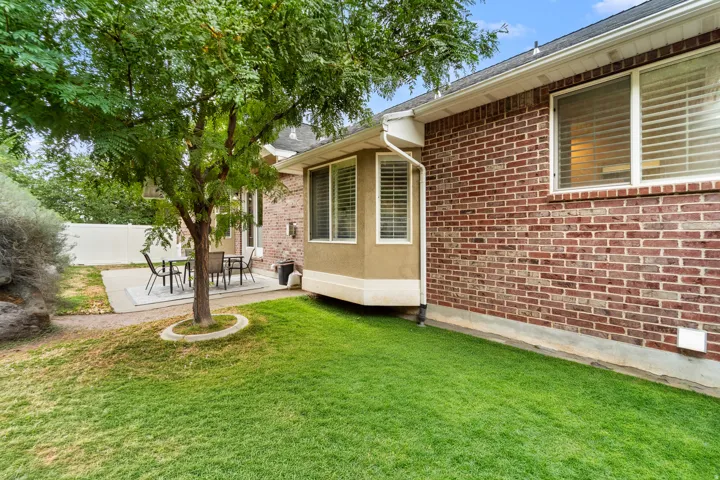 Manicured lawn with mature tree, concrete patio, brick exterior, and bay window