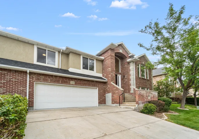 Brick facade with a two-car garage, concrete driveway, and established landscaping