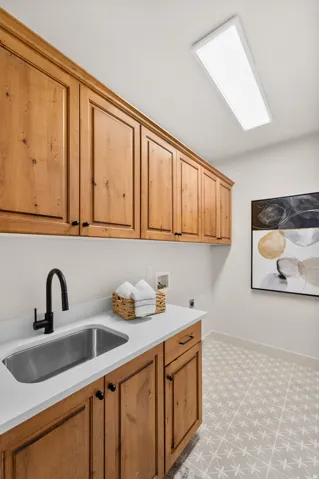 Wood-finish cabinetry, stainless steel sink, solid surface countertop, matte black faucet, and patterned floor tile