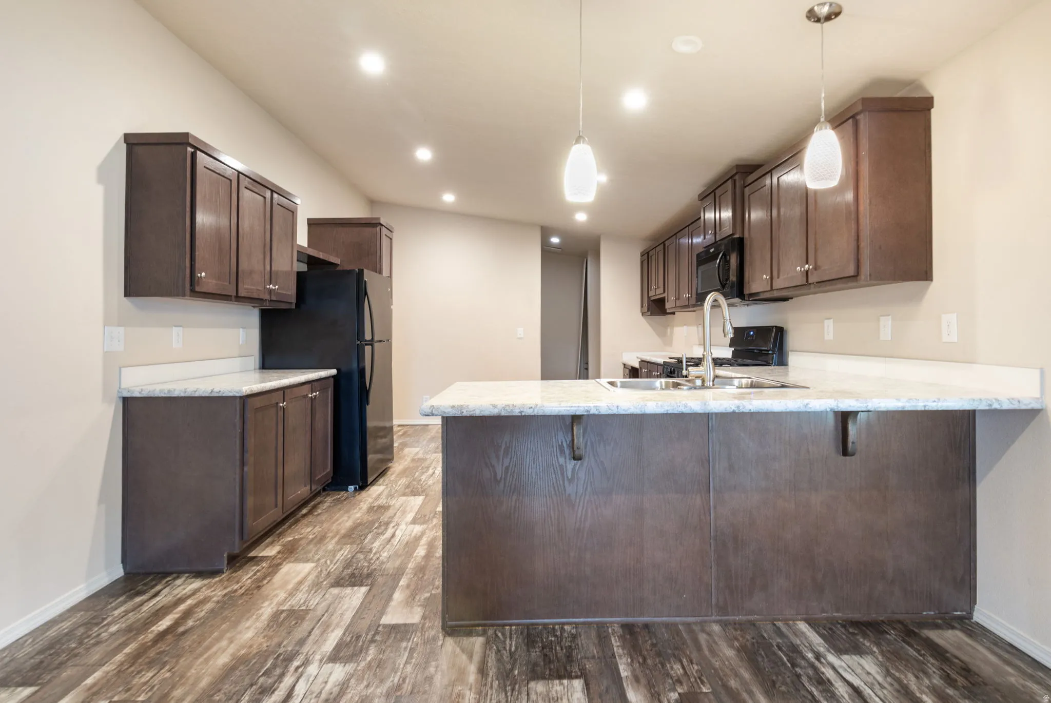 Kitchen featuring dark wood-finish cabinetry, light-toned countertops, a central island with bar seating, wood-finish flooring, and recessed and pendant lighting