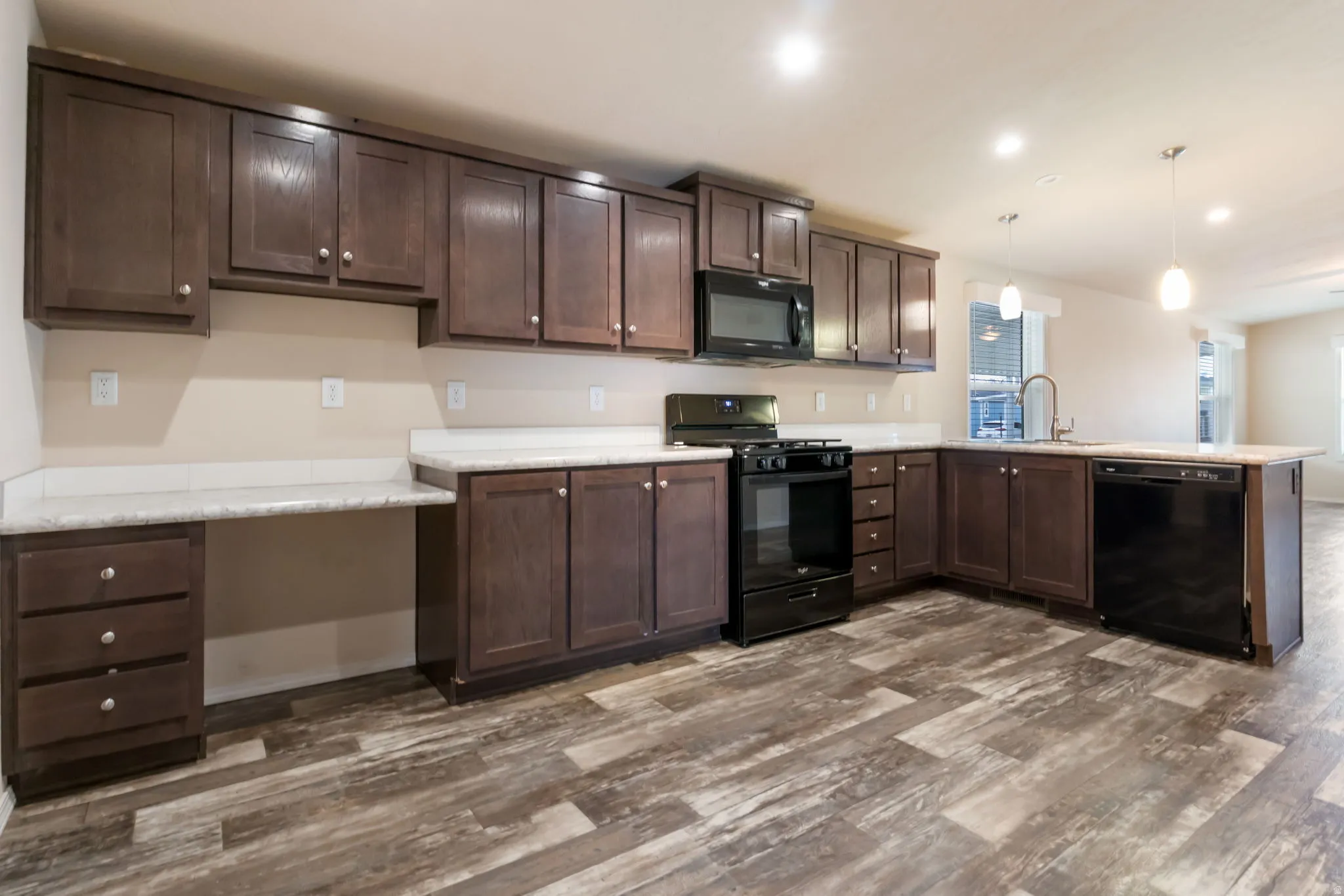 Expansive kitchen featuring dark wood cabinetry, light countertops, black appliances, and wood-finish flooring