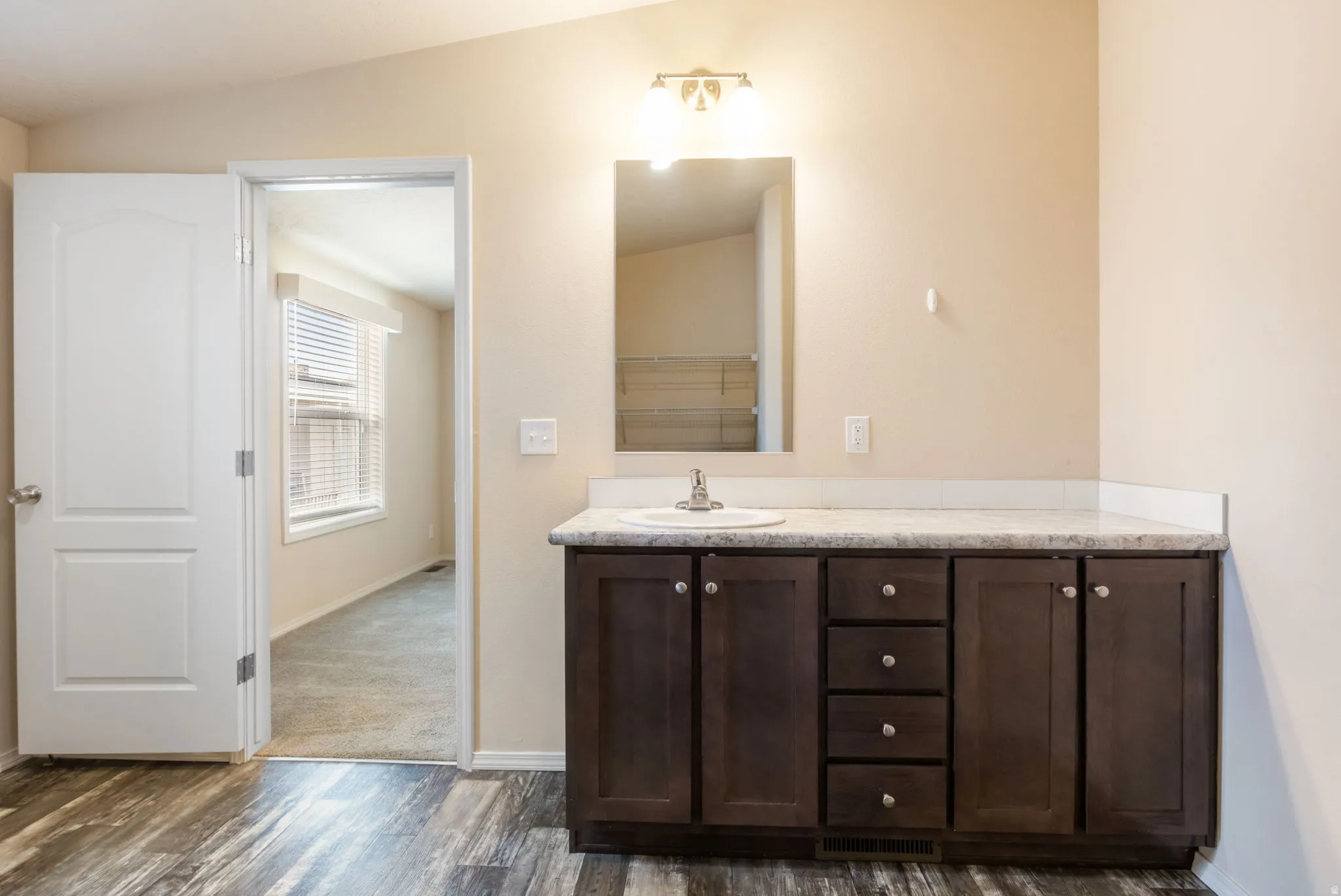 Wood-finish flooring, dark wood vanity with ample storage, white countertop, integrated sink, and overhead lighting fixture