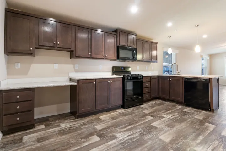 Expansive kitchen featuring dark wood cabinetry, light countertops, black appliances, and wood-finish flooring