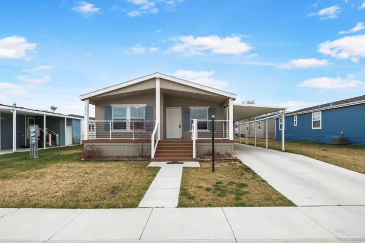 Front exterior featuring a covered porch with railing, dedicated carport, concrete driveway, and front lawn