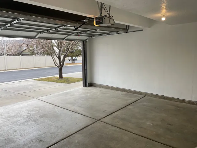 Concrete flooring with perimeter base trim, automatic overhead garage door, and ceiling-mounted lighting