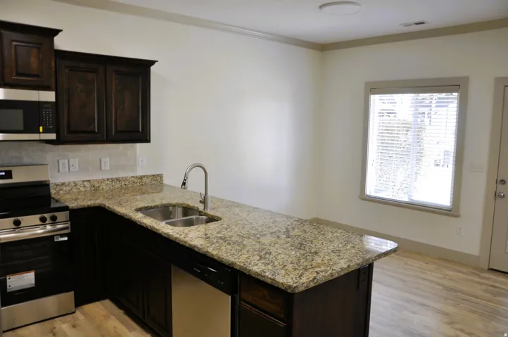 Kitchen featuring dark wood cabinetry, stainless steel appliances, a dual basin sink, speckled countertops, and wood-finish flooring