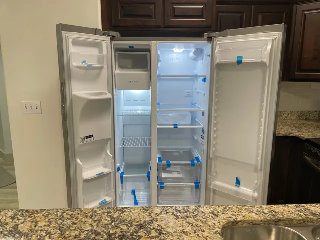 Stainless steel side-by-side refrigerator featuring an internal ice maker, dark wood-finish cabinetry, speckled countertop, and a stainless steel sink