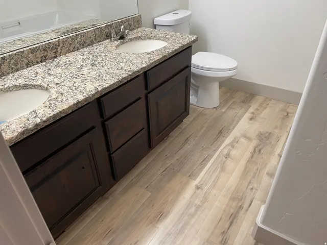 Dual vanity with granite countertop, integrated sinks, wood-finish cabinetry, and wood-finish flooring