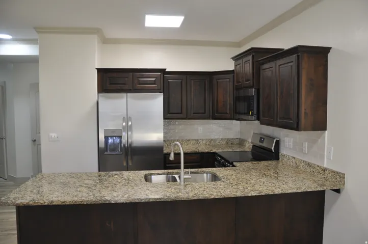 Kitchen featuring dark wood cabinetry, stainless steel appliances, a stainless steel sink with a gooseneck faucet, light-toned stone countertops, and a subway tile backsplash