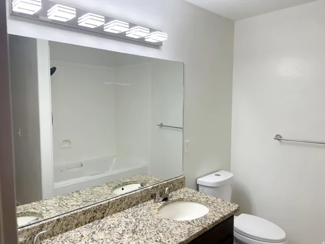 Granite-finish countertop with integrated sink, dark wood-finish vanity, and a full-width mirror