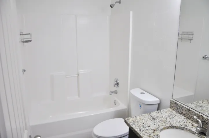 Bathtub with integrated shower, chrome fixtures, and a white toilet