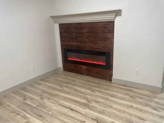 Contemporary electric fireplace with wood-finish accent wall, crown molding, and wood-finish flooring