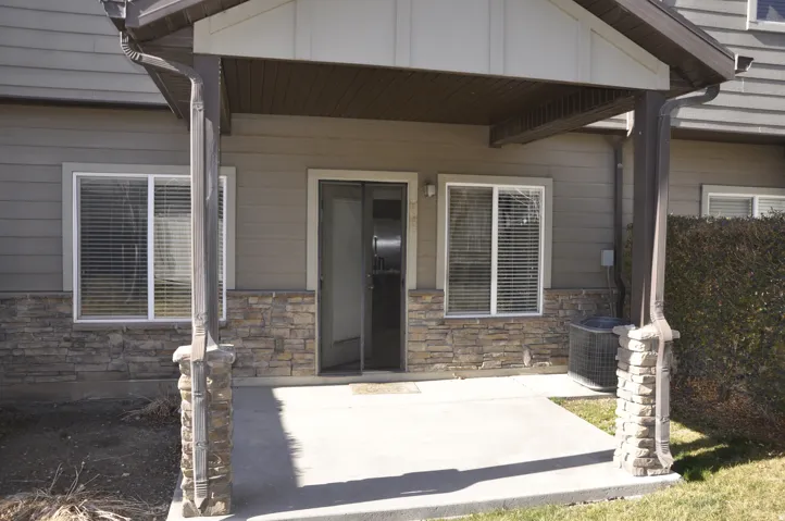 Covered concrete patio with stone-wrapped columns, vinyl siding, and a sliding glass door