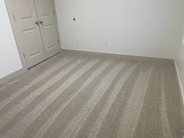 Wall-to-wall carpeting with striped texture, white painted walls, and light-colored trim