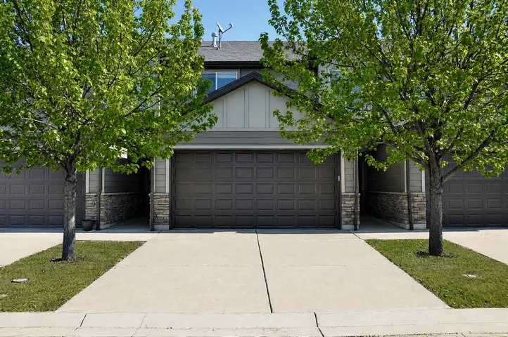 Townhome exterior featuring a paneled garage door, stone accents, and light-colored siding