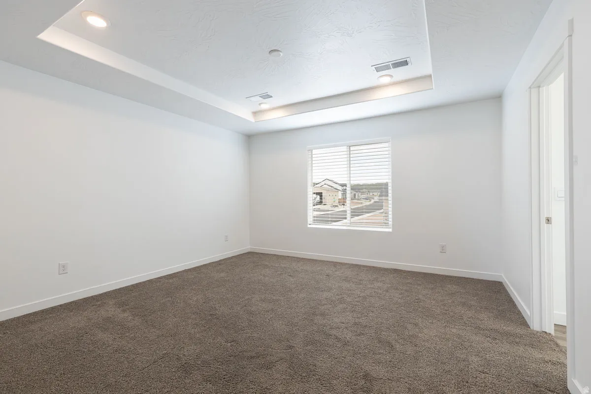 Recessed ceiling with integrated lighting, neutral wall paint, textured carpeting, and window blinds