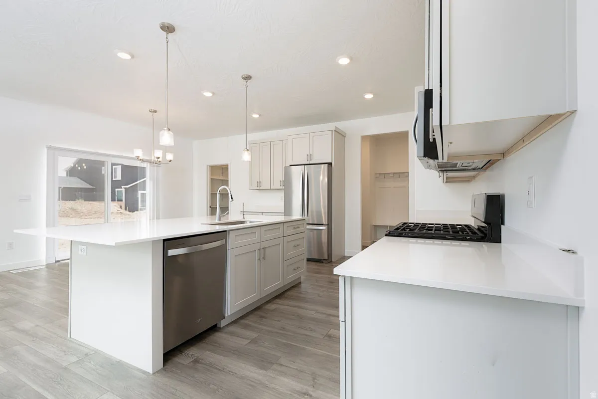 Contemporary kitchen featuring white cabinetry, stainless steel appliances, quartz countertops, a large center island with waterfall edge, pendant lighting, recessed ceiling lights, gas cooktop with range hood, and wood-finish flooring throughout the open