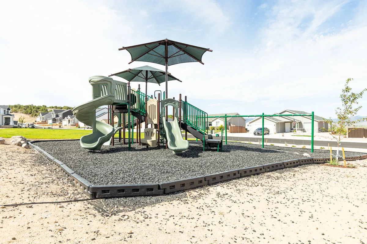 Outdoor playground structure featuring multiple slides, swings, and shade coverings over rubberized surfacing