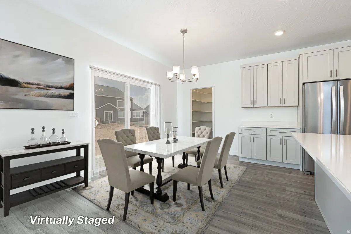 Wood-finish flooring, white walls, and a contemporary chandelier illuminate this space featuring light gray cabinetry, white countertops, and a built-in pantry with shelving