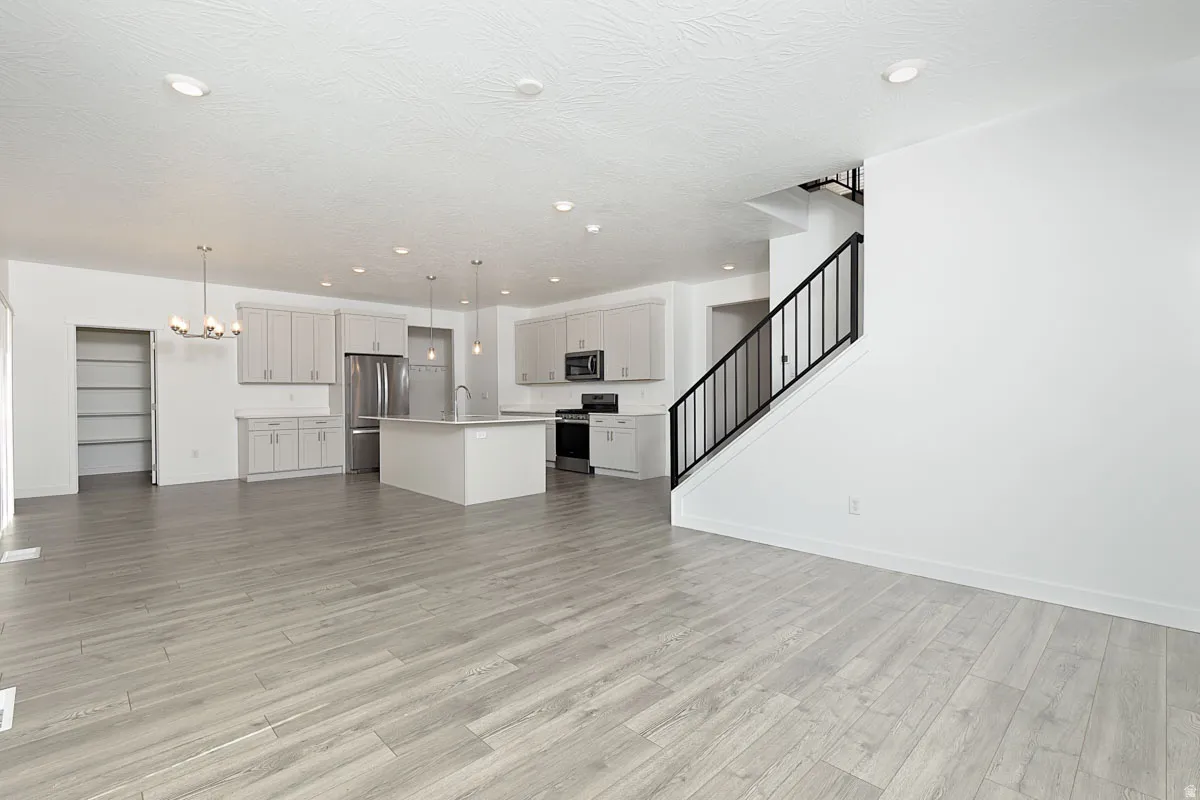 Open-concept living area featuring wood-finish flooring, a modern kitchen with a central island, stainless steel appliances, light cabinetry, and a staircase with wrought iron railing