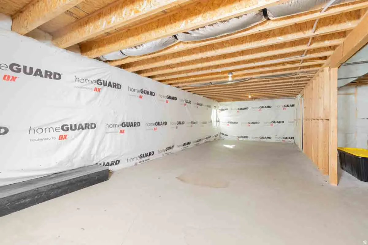 Unfinished basement with concrete flooring, exposed wood ceiling joists, and framed partition walls