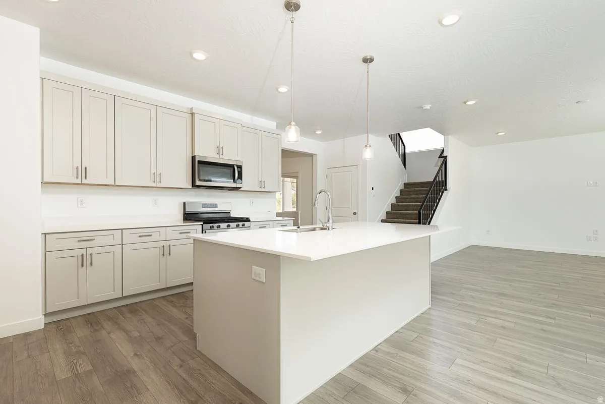 Kitchen featuring light-toned cabinetry, stainless steel appliances, a large center island with a sink, and pendant lighting