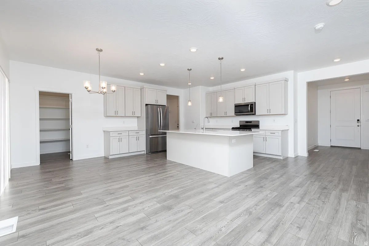 Spacious open-concept kitchen with wood-finish flooring, white cabinetry, a large kitchen island, and stainless steel appliances