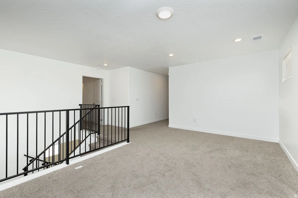 Open landing area featuring gray carpet flooring, white walls, black metal railings, and recessed lighting