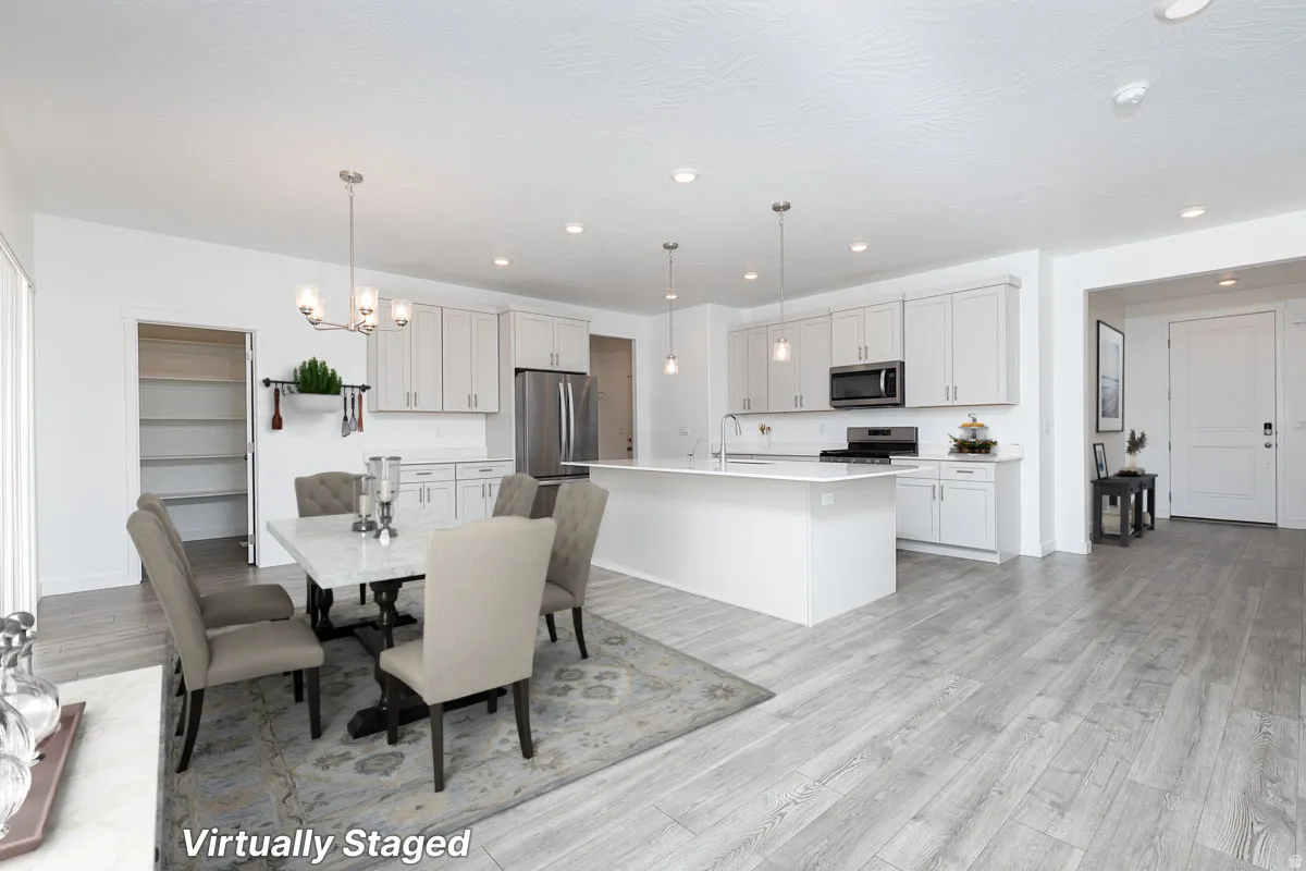 Open-concept kitchen and dining area featuring light-toned cabinetry, stainless steel appliances, a center island with sink, and wood-finish flooring