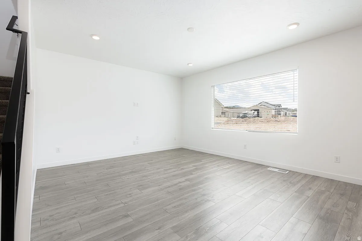 Spacious room featuring wood-finish flooring, recessed lighting, and a large window with blinds