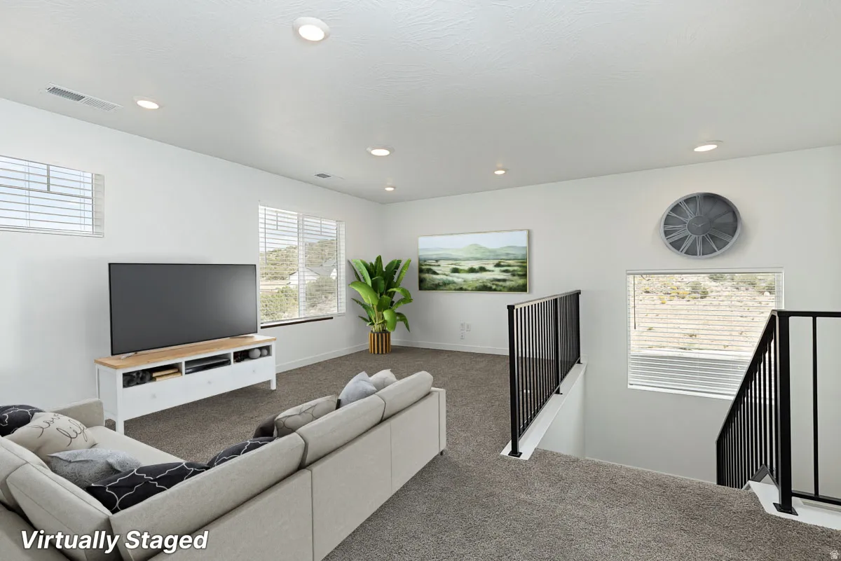 Spacious recreation room featuring recessed ceiling lighting, large flat-screen TV mounted above a built-in media console with wood-finish shelving, and plush seating arrangement