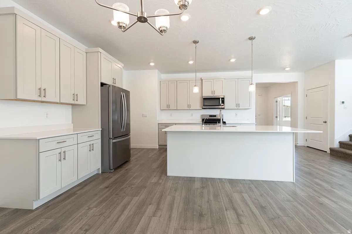 Contemporary kitchen featuring light wood-finish flooring, white cabinetry, a large island with an extended countertop, stainless steel appliances, and recessed lighting