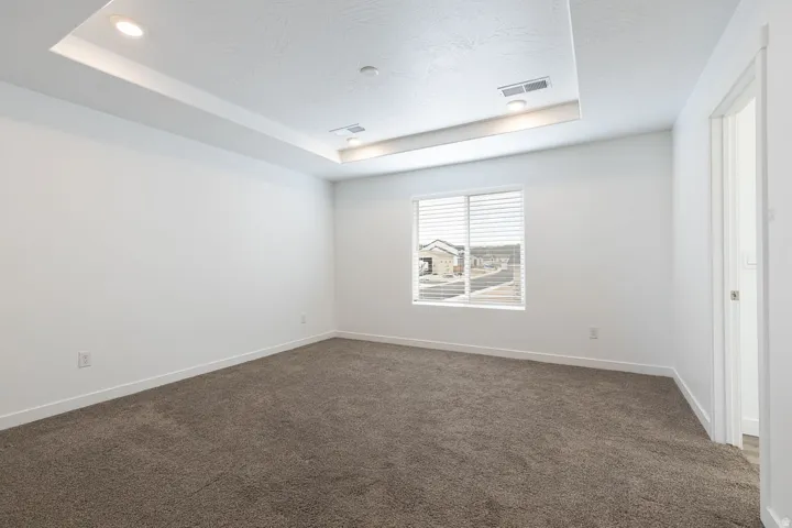 Recessed ceiling with integrated lighting, neutral wall paint, textured carpeting, and window blinds