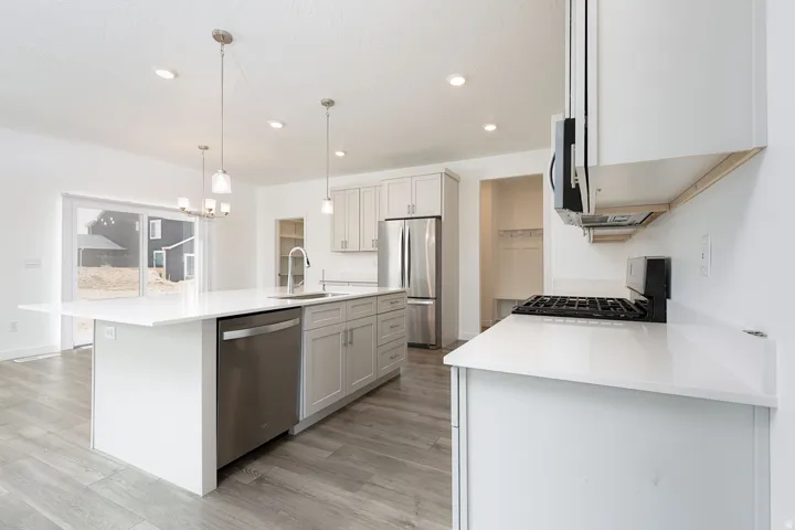 Contemporary kitchen featuring white cabinetry, stainless steel appliances, quartz countertops, a large center island with waterfall edge, pendant lighting, recessed ceiling lights, gas cooktop with range hood, and wood-finish flooring throughout the open