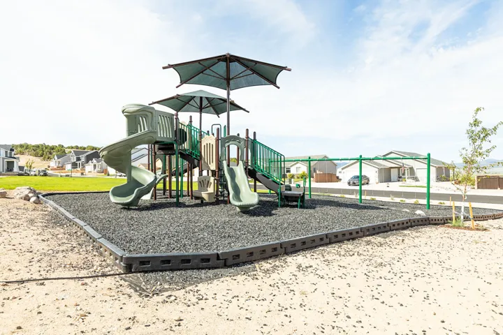 Outdoor playground structure featuring multiple slides, swings, and shade coverings over rubberized surfacing