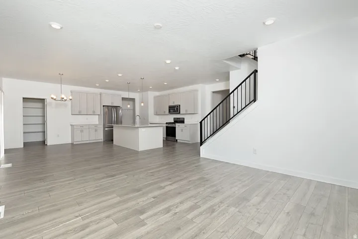 Open-concept living area featuring wood-finish flooring, a modern kitchen with a central island, stainless steel appliances, light cabinetry, and a staircase with wrought iron railing