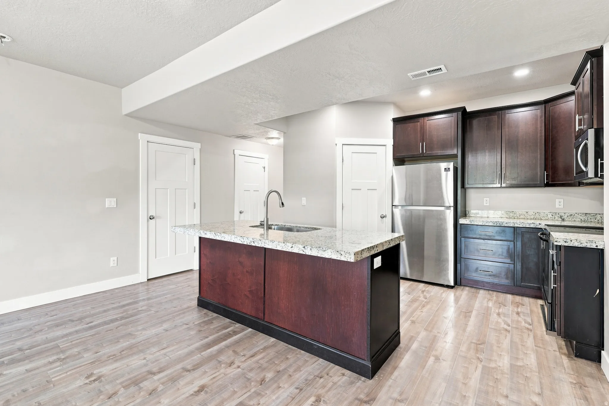 Kitchen island with granite countertop, stainless steel appliances, dark wood cabinetry, and light wood-finish flooring