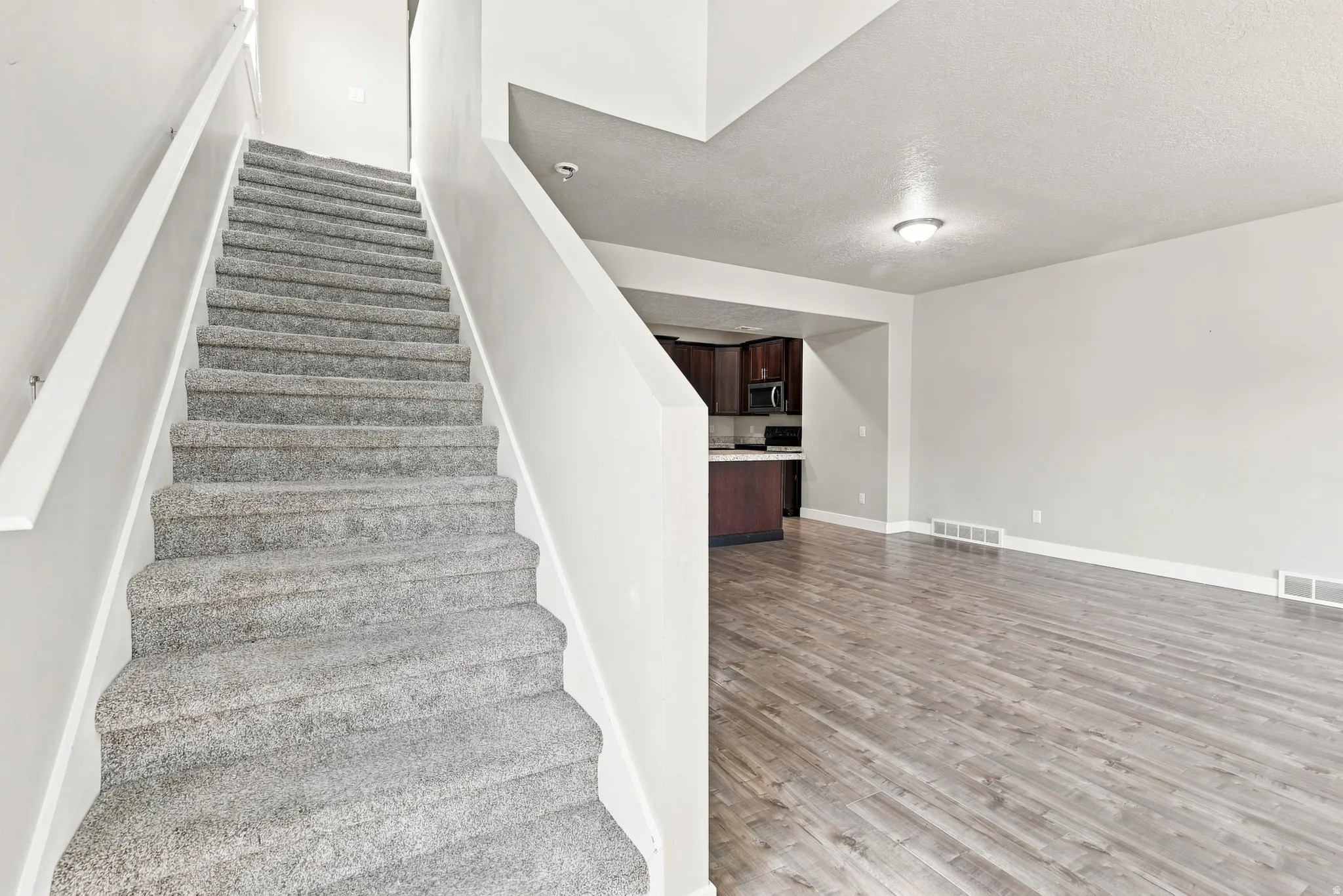 Carpeted staircase with white handrails, wood-finish flooring, recessed ceiling lighting, and a kitchen featuring wood cabinetry and white countertops