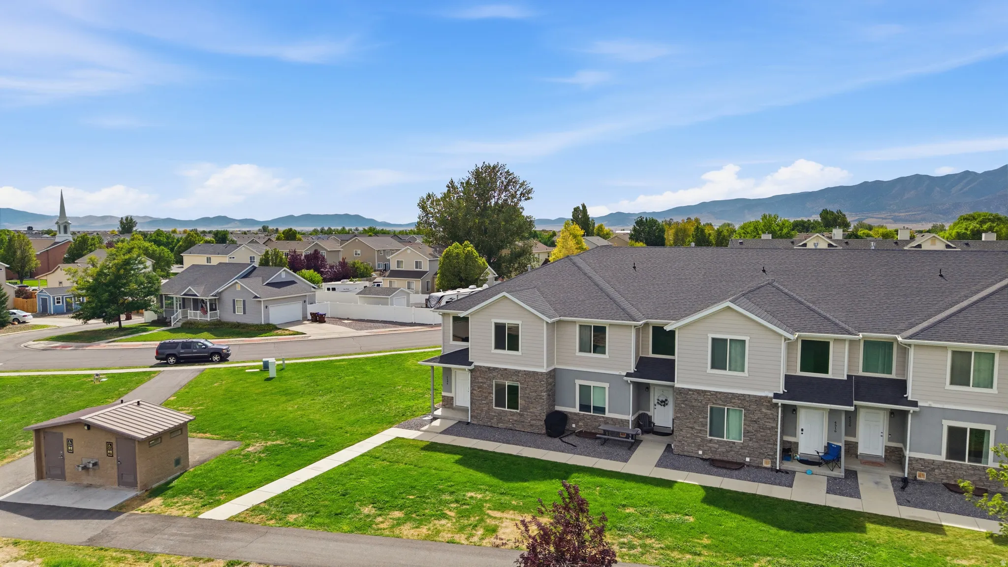 Townhome exterior featuring gray siding, stone veneer accents, and a dark shingle roof