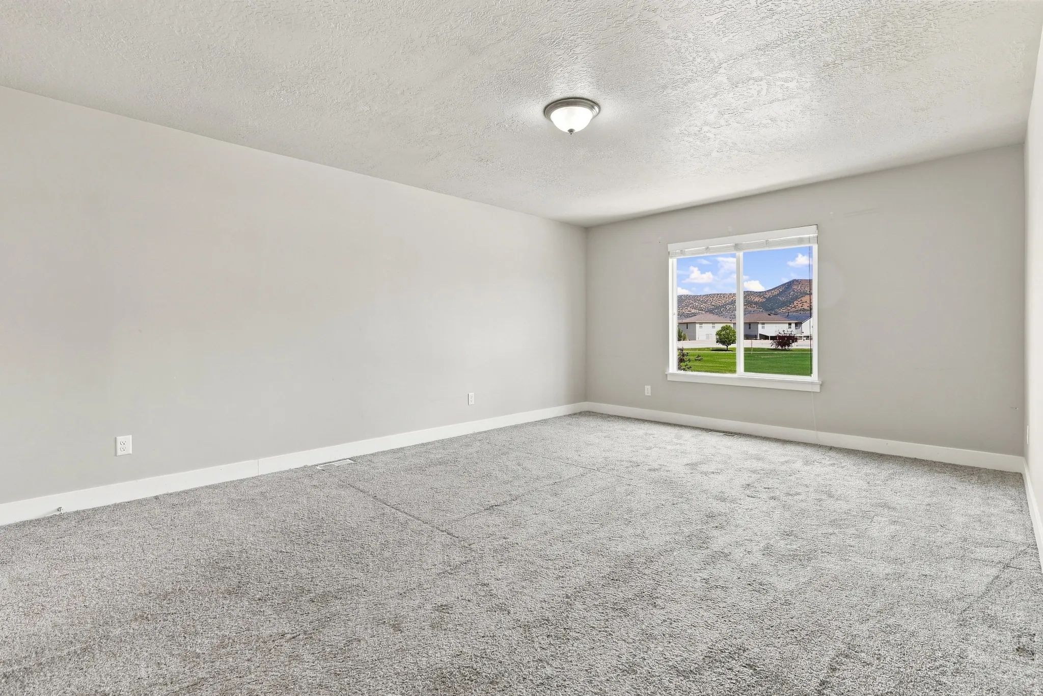 Neutral-toned walls with grey carpeting, featuring a window with exterior scenery