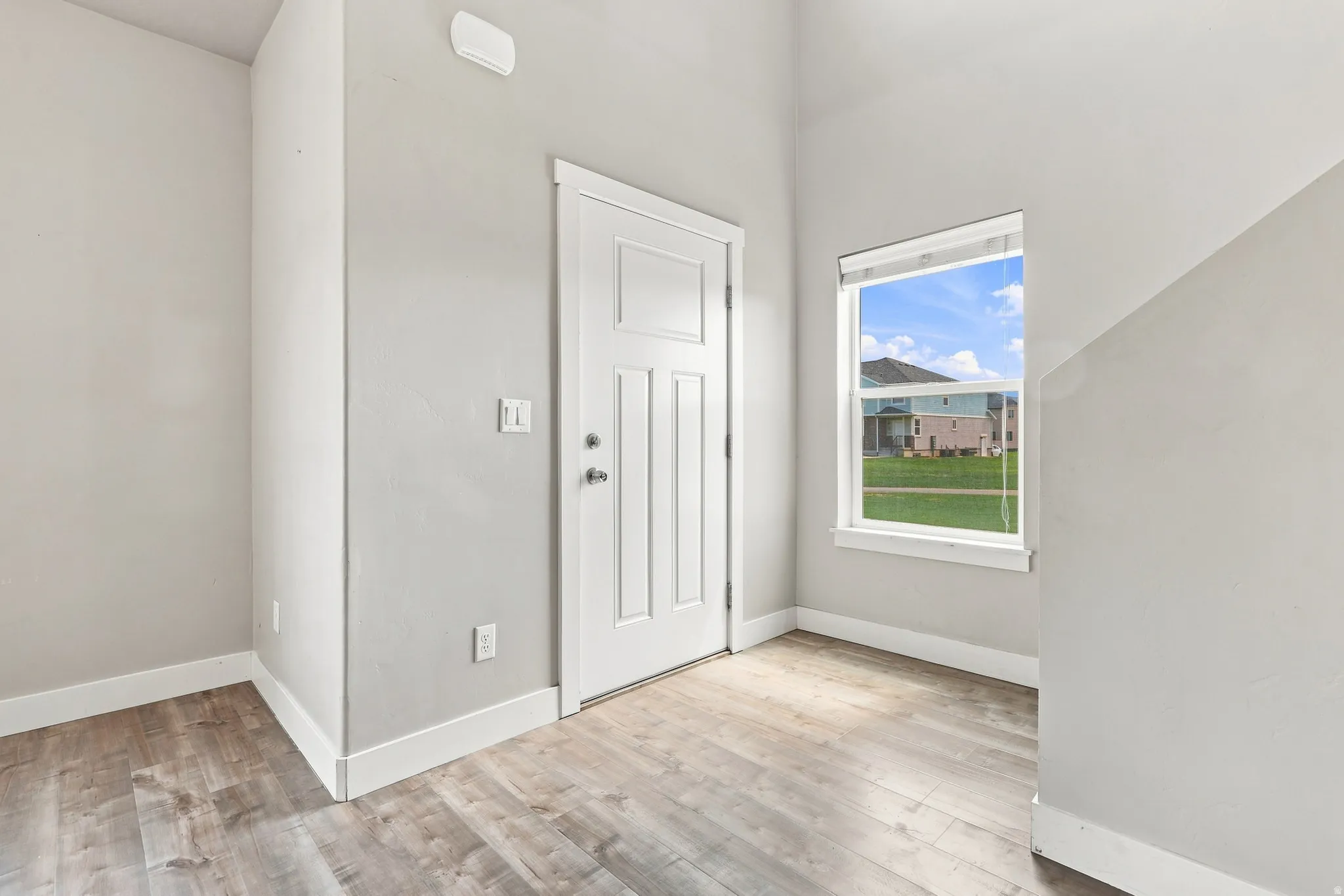 Wood-finish flooring, white paneled door, and a single window offering natural illumination