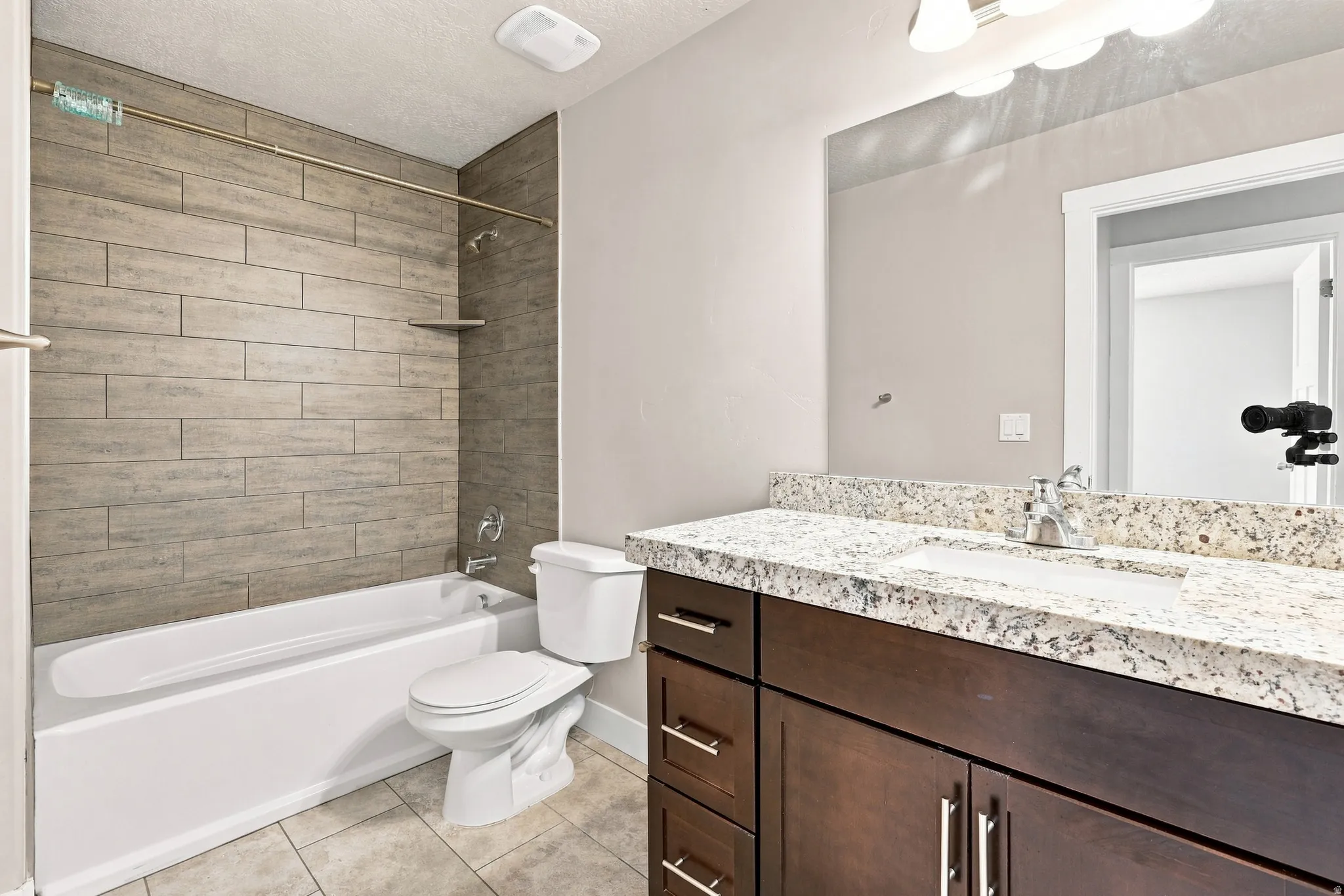 Full bathroom featuring a single vanity with stone countertop, dark wood-finish cabinetry, and an integrated white sink