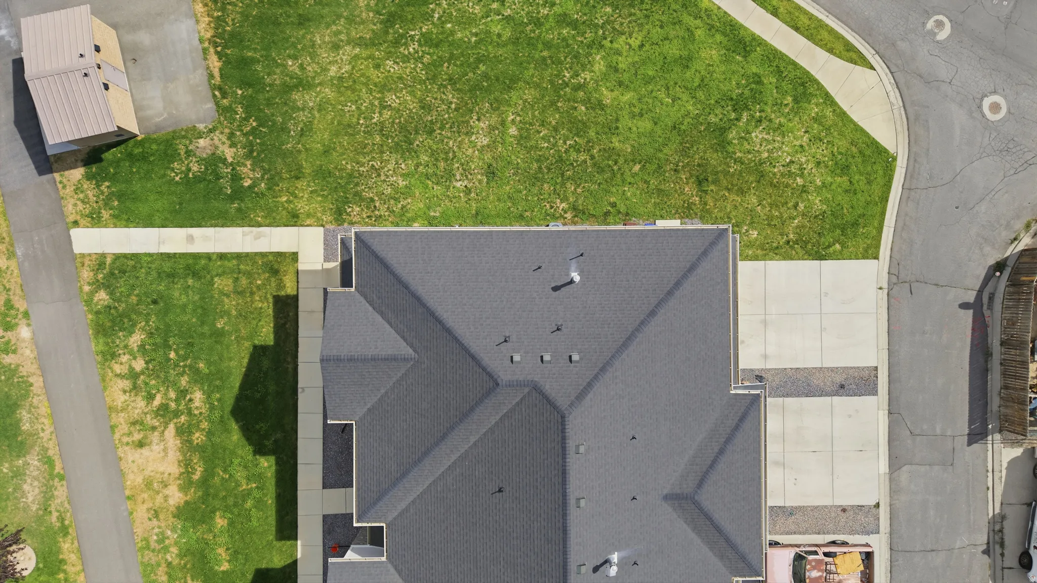 Asphalt shingle roofing, paved driveway, concrete sidewalks, and a detached shed