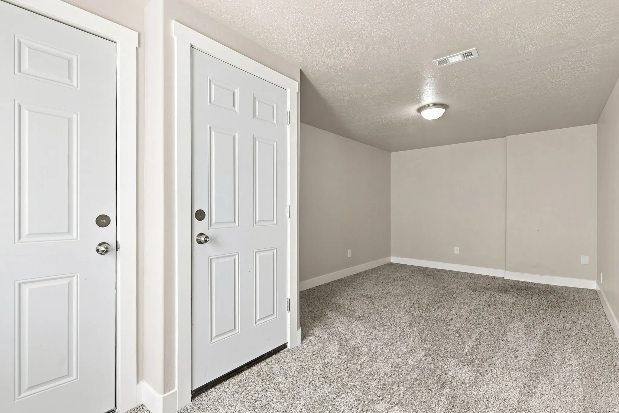 Two paneled doors with chrome hardware, neutral wall paint, textured ceiling, flush mount ceiling fixture, and carpeted flooring