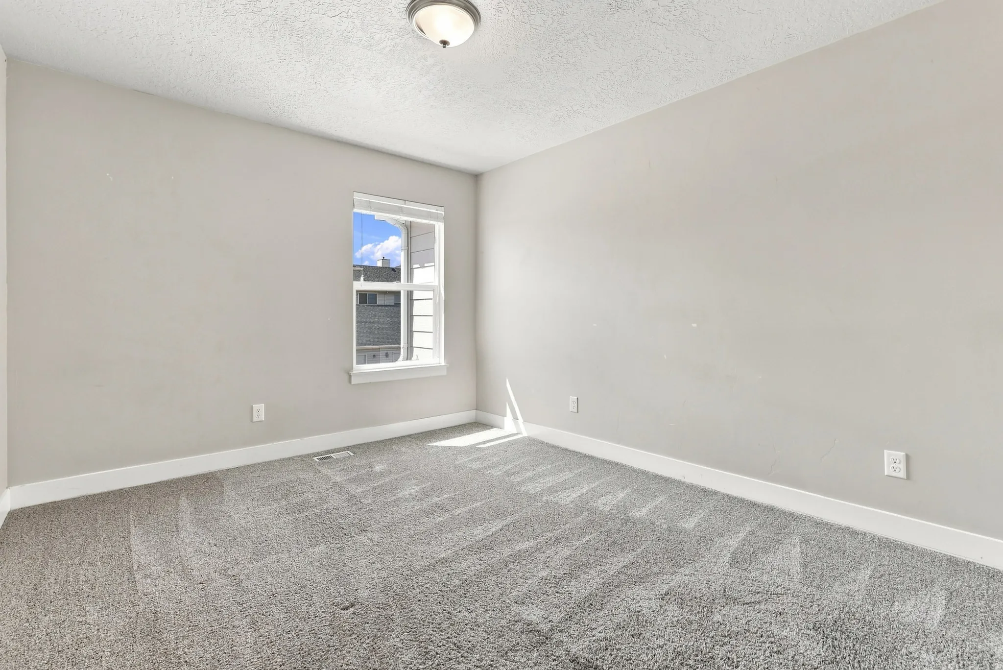 Neutral wall paint, gray patterned carpeting, and a window with white trim