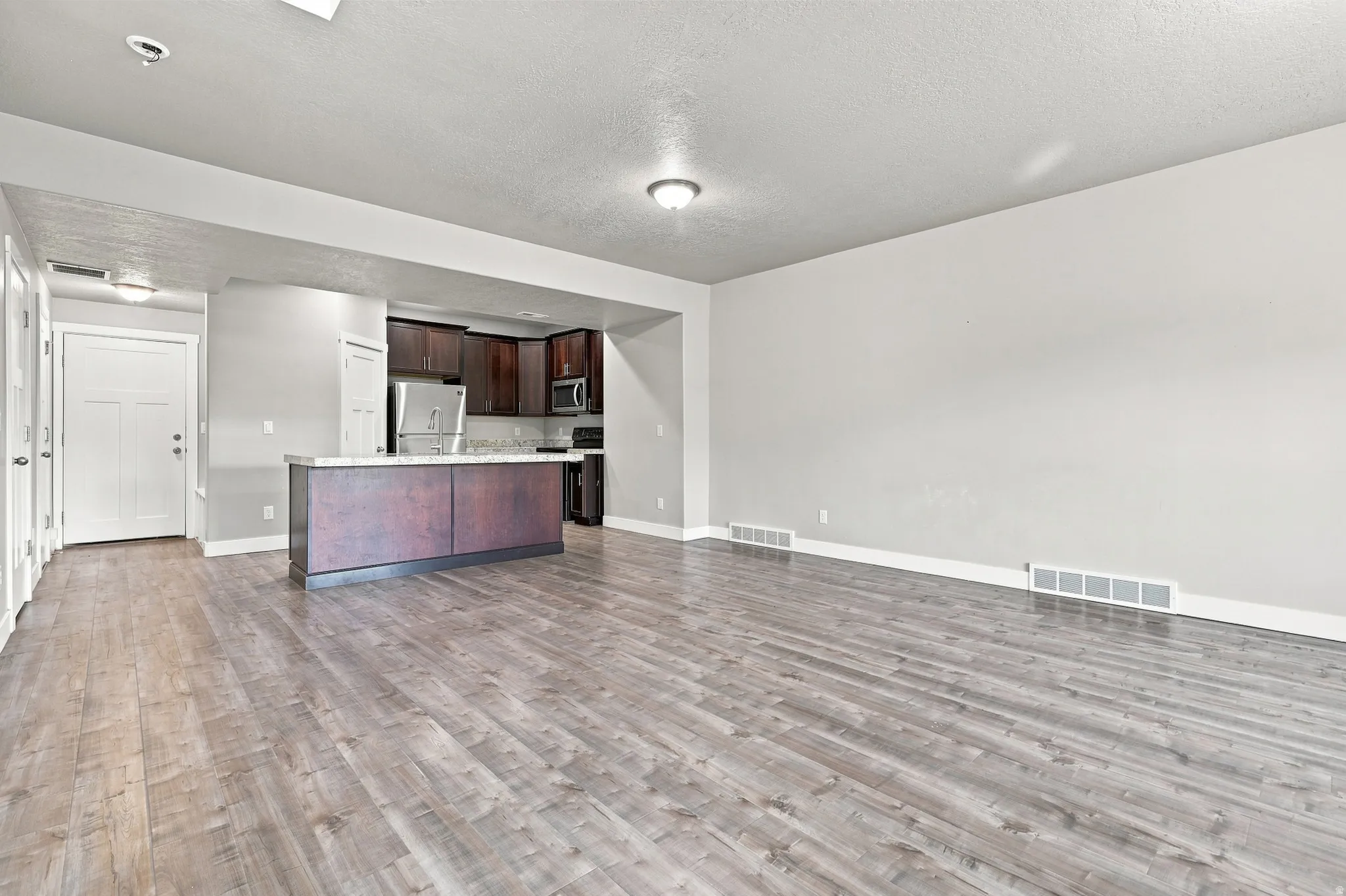 Open-concept living area featuring wood-finish flooring, recessed lighting, a kitchen island with a stone-look countertop, dark wood cabinetry, and stainless steel appliances